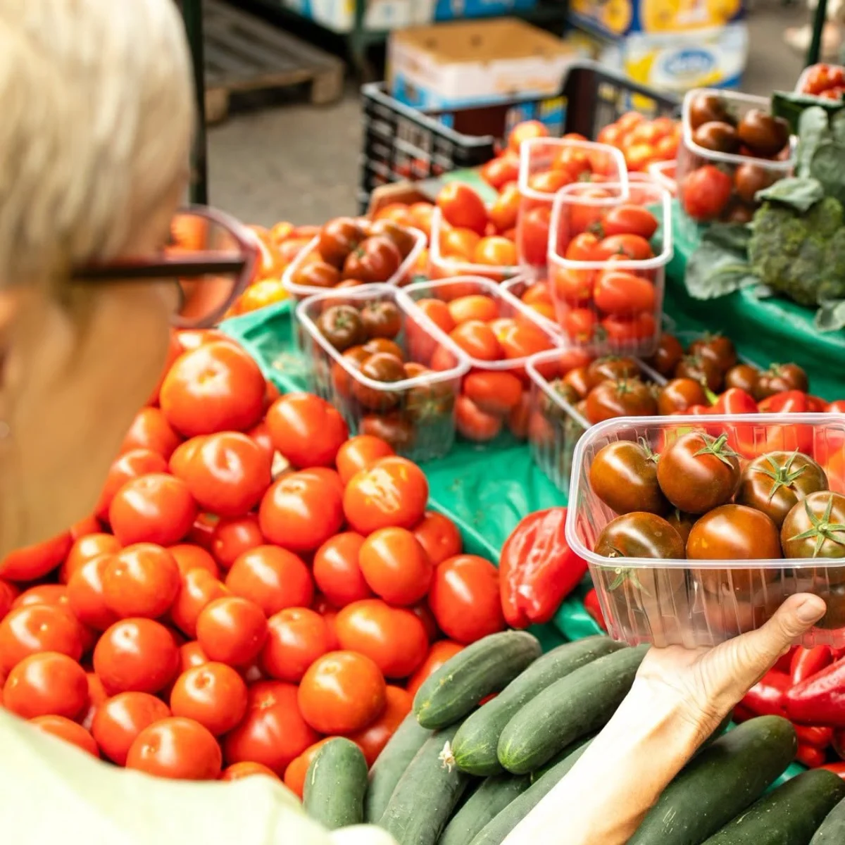 courses avec une dame qui regarde des tomates ainsi que d'autre légumes